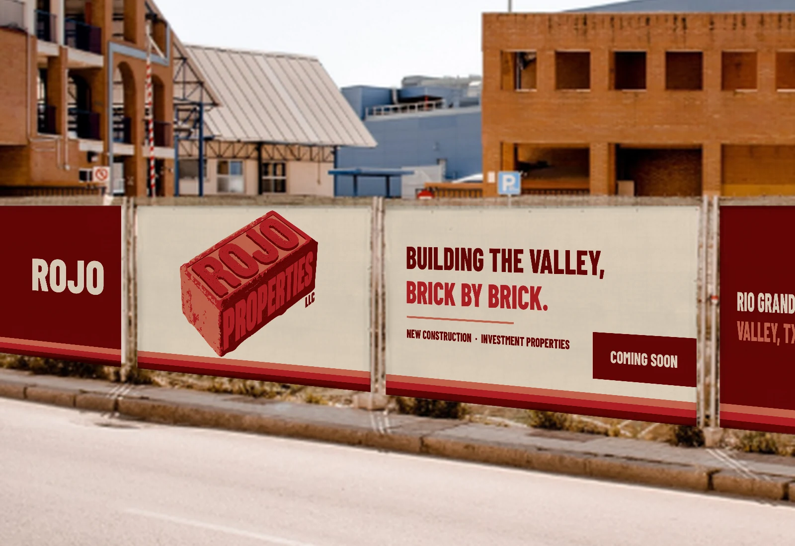 Row of Rojo Properties banners on construction fence panels along a street, with the brick logo and the line Building the Valley, Brick by Brick